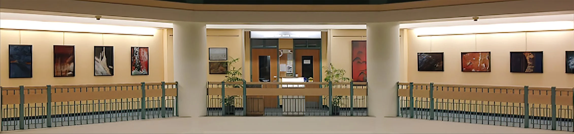 Interior of a building with art prints on the walls, a railing in the foreground, and a small counter or reception area in the background.