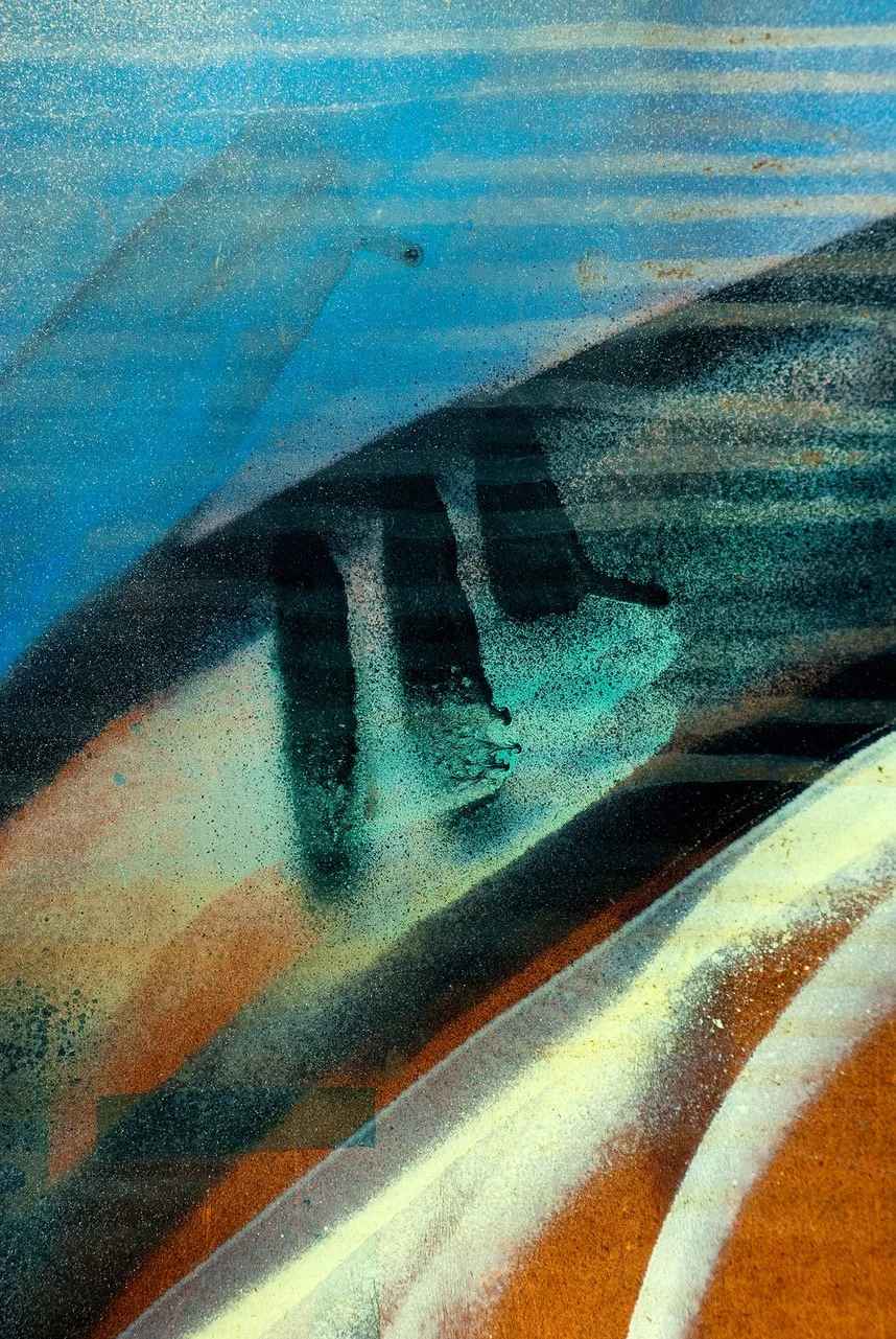 Close-up of a spray-painted mural featuring a woman's face with dark hair, set against abstract colorful background with blue, orange, and brown tones.
