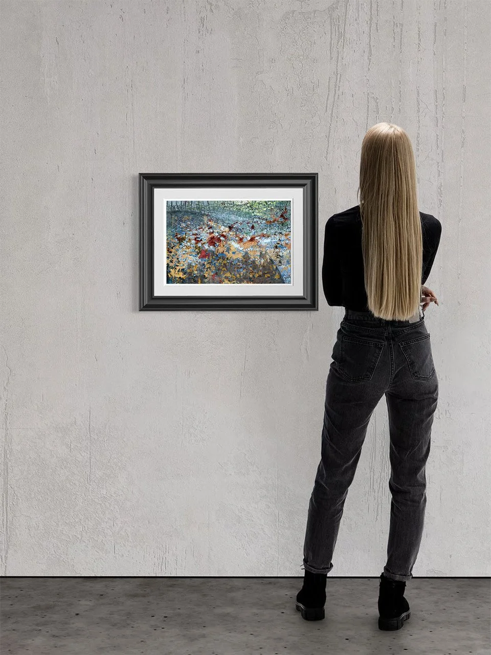 A woman with long blonde hair, wearing a black top and dark jeans, stands in front of a framed painting in an art gallery, looking at the artwork.
