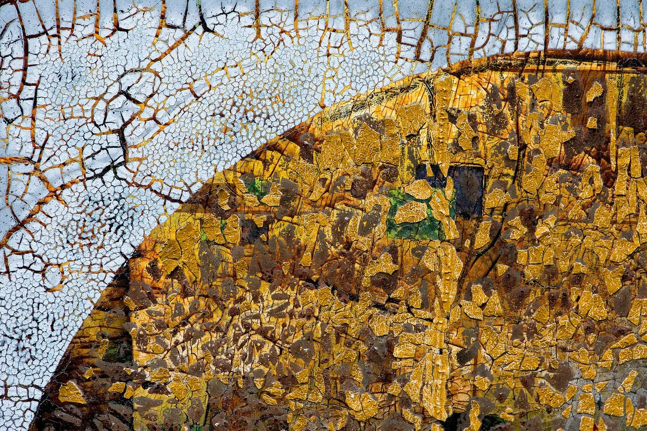 Close-up of a weathered, cracked surface with peeling paint in white and yellowish-brown colors.