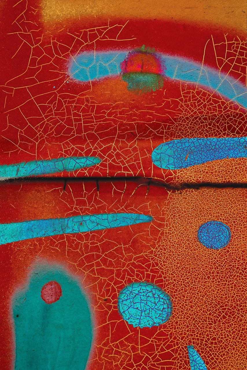 Abstract graffiti art featuring blue, green, and red shapes with yellow cracks on a rusty red background.