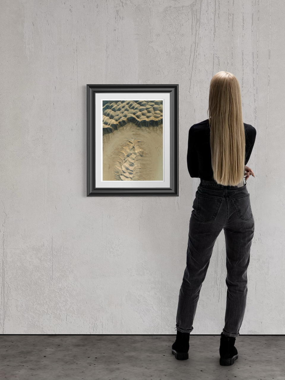 A woman with long blonde hair stands in front of a framed abstract artwork on a concrete wall.