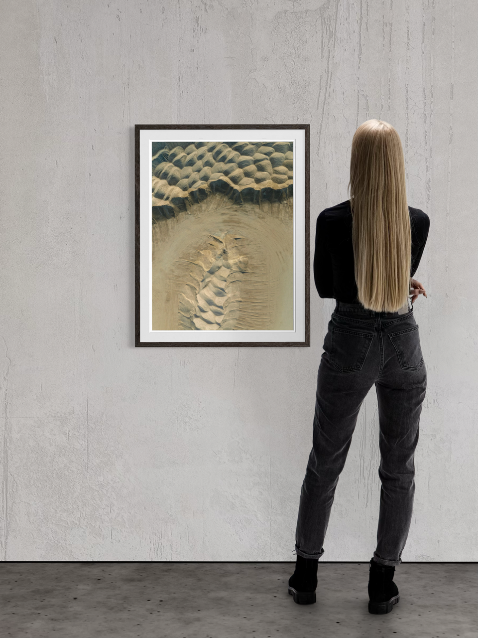 A woman with long blonde hair wearing a black jacket and jeans viewing an abstract painting in a gallery.