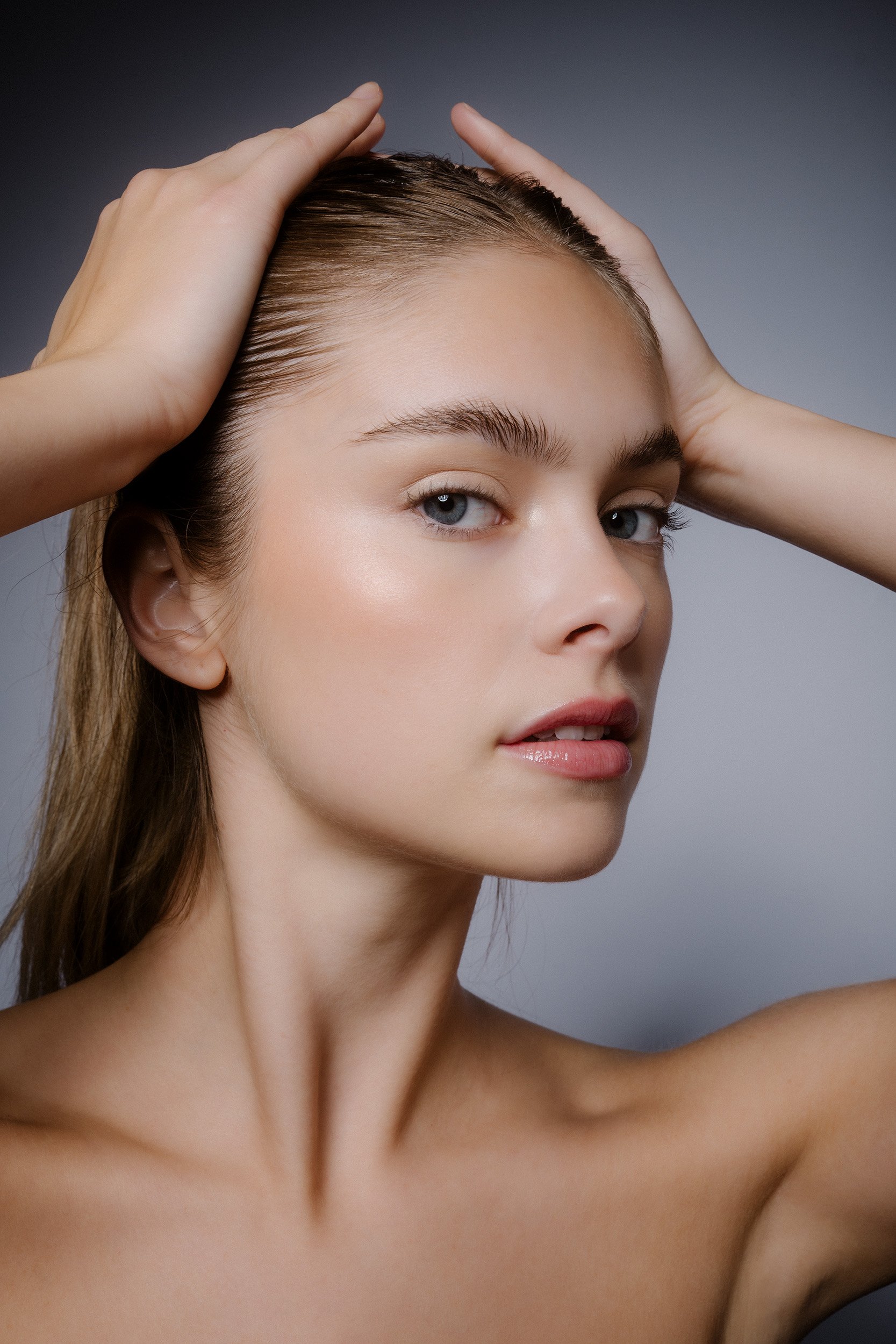 Nahaufnahme eines jungen Frauengesichts mit blauen Augen, braunen Haaren und natürlichem Make-up, die ihre Haare zurückstreicht.