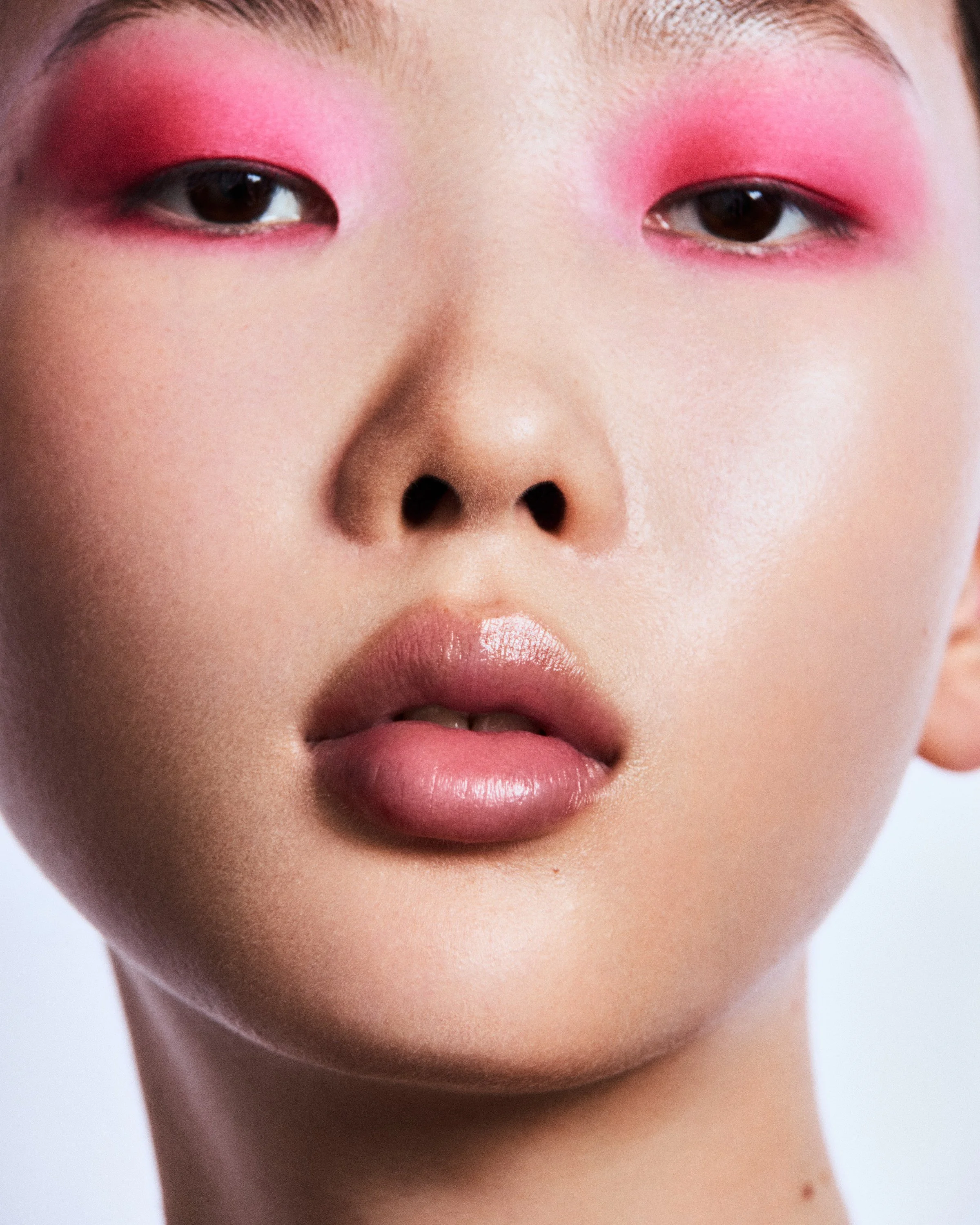 Nahaufnahme eines Gesichts mit pinkem Make-up um die Augen und auf den Lippen, sowie gepflegter Haut.