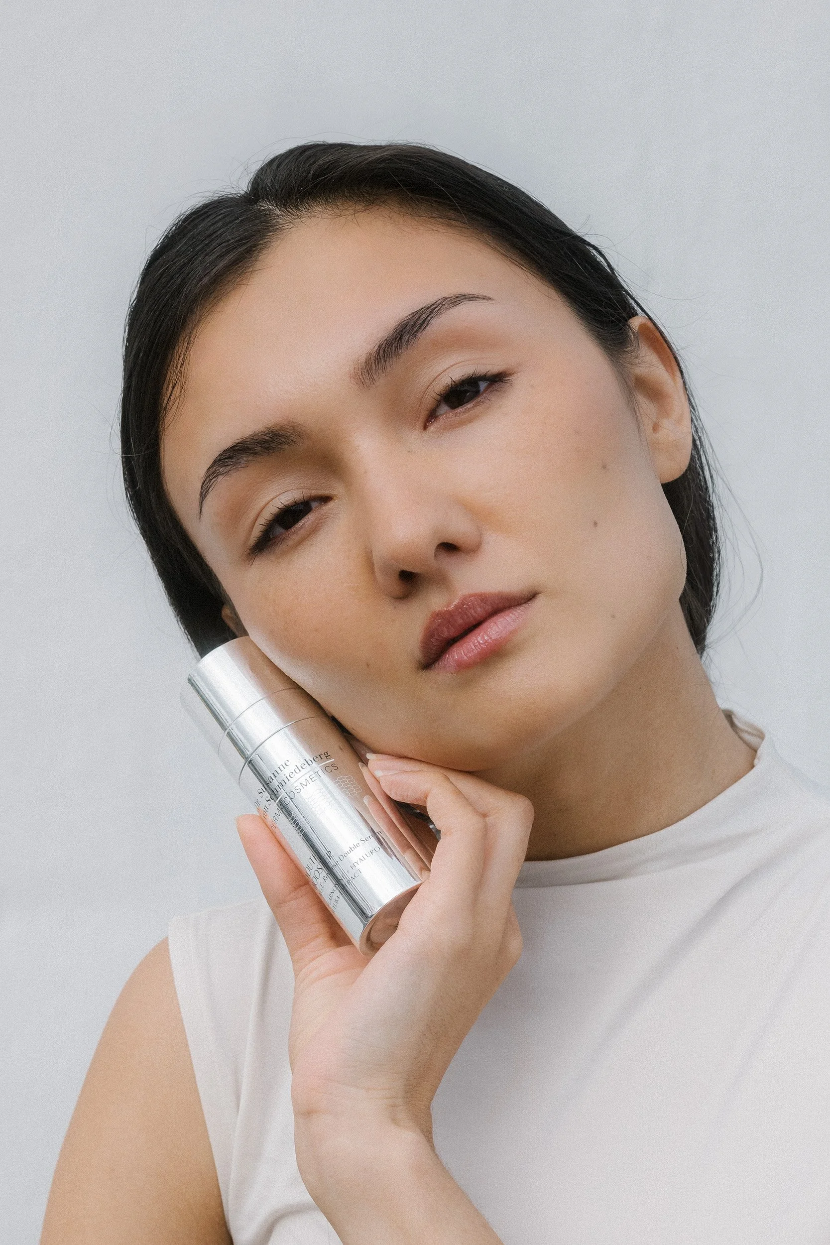 Nahaufnahme eines jungen asiatischen Mädchens mit dunklem Haar, das ein silbernes Kosmetikprodukt hält und auf die Kamera blickt.