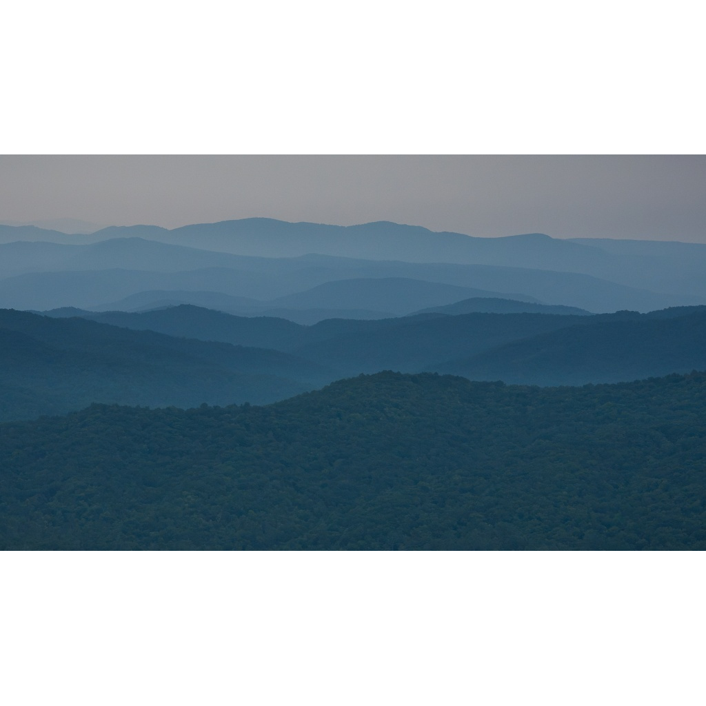 Blue-toned Appalachian mountain ridges recede into the distance beneath a soft, open sky, with each layer fading gently into haze and a dark green foreground ridge anchoring the scene.