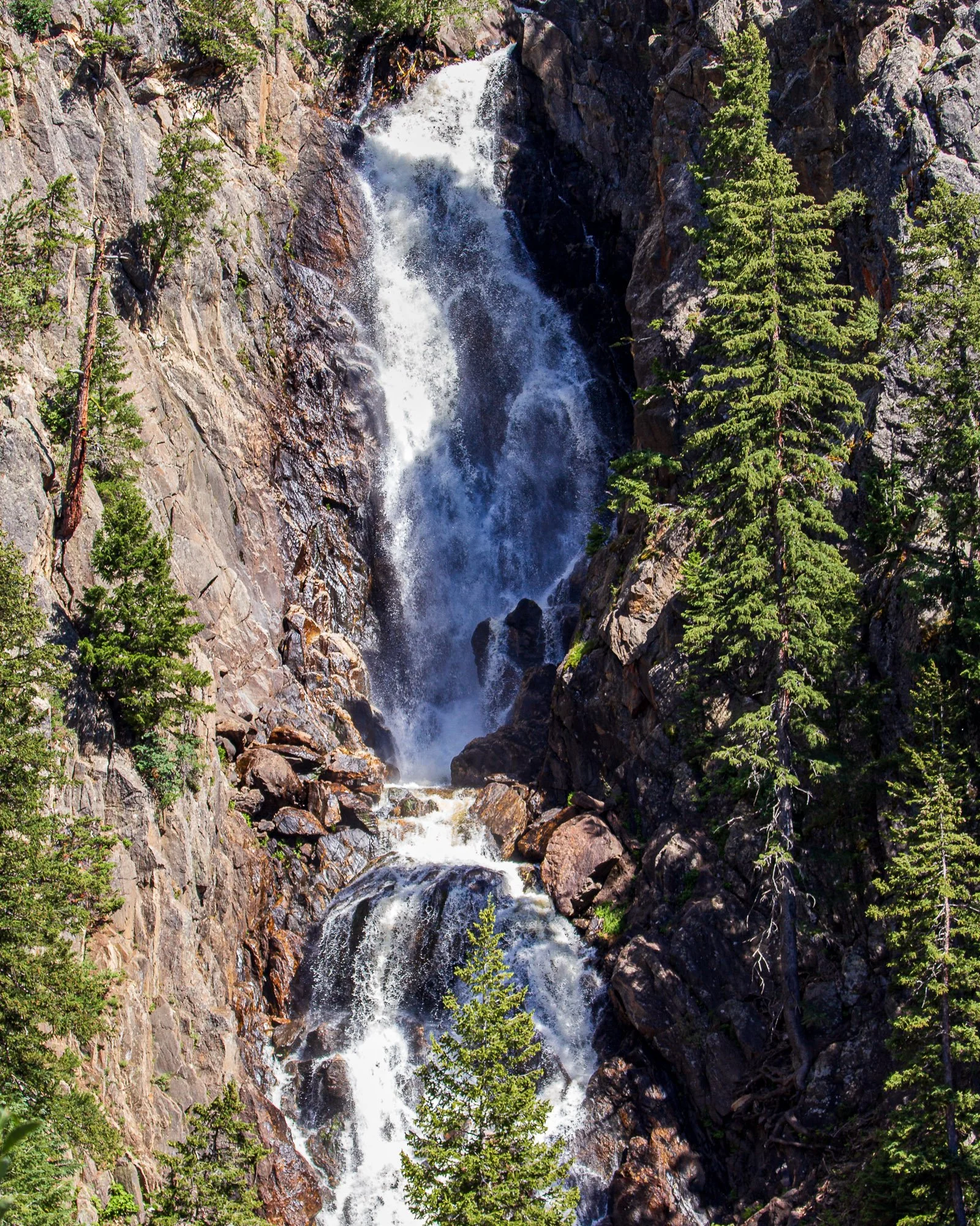 Multi-tiered mountain waterfall cascading between steep rock walls and evergreen trees near Steamboat Springs, Colorado.