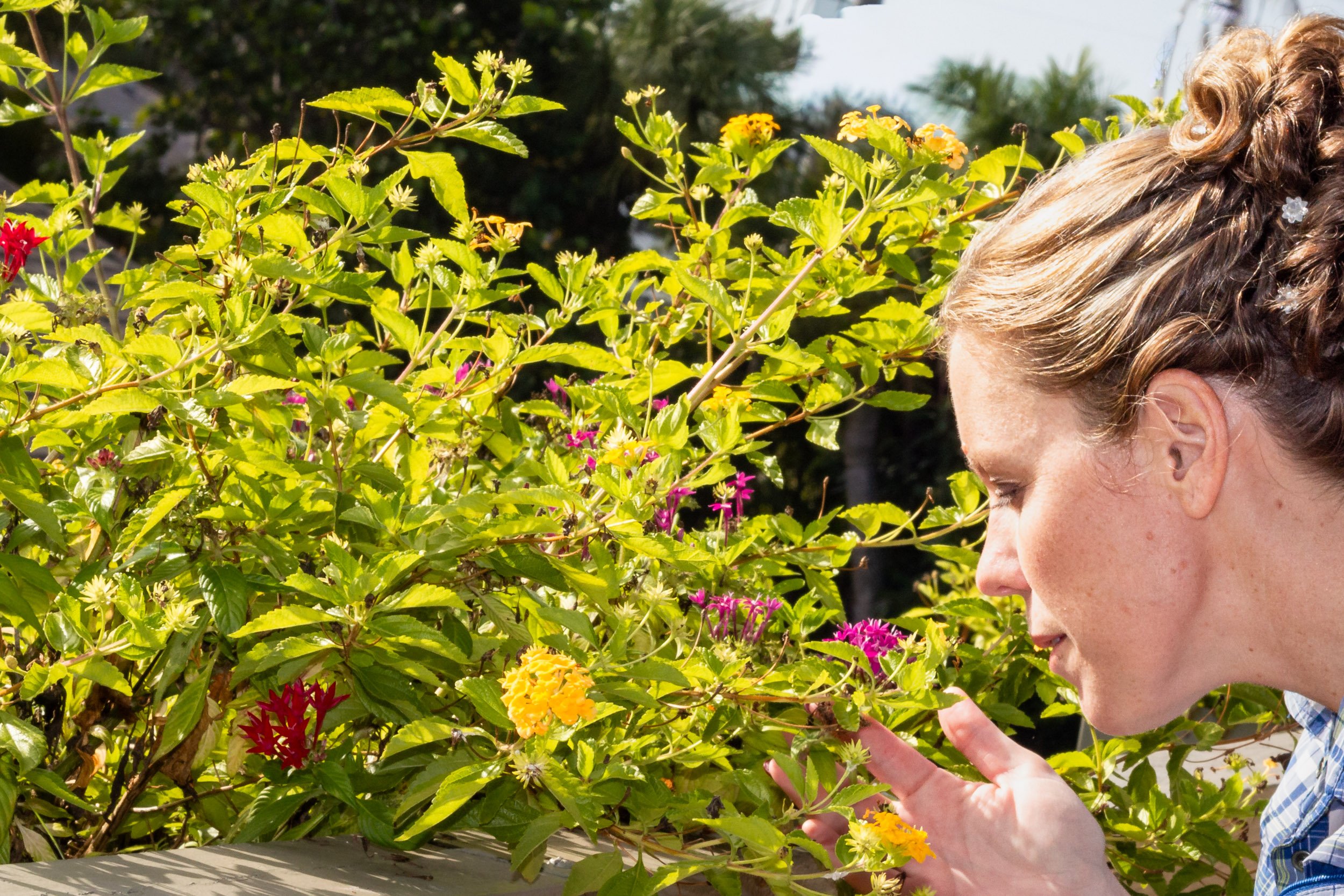 Portrait of photographer Leigh Anne Brewster closely observing blooming flowers in a garden.