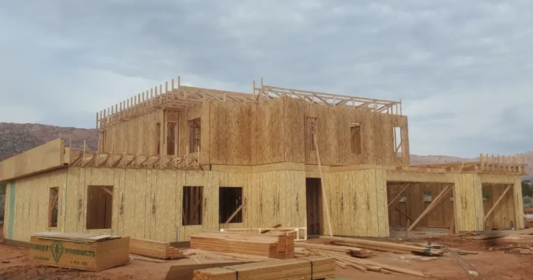 Wooden framing of a two-story house under construction with building materials on the ground.