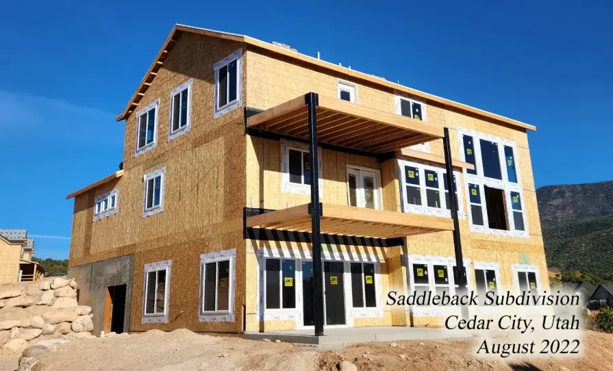 A multi-story house under construction with wood framing and windows installed, located in Saddleback Subdivision, Cedar City, Utah, in August 2022.