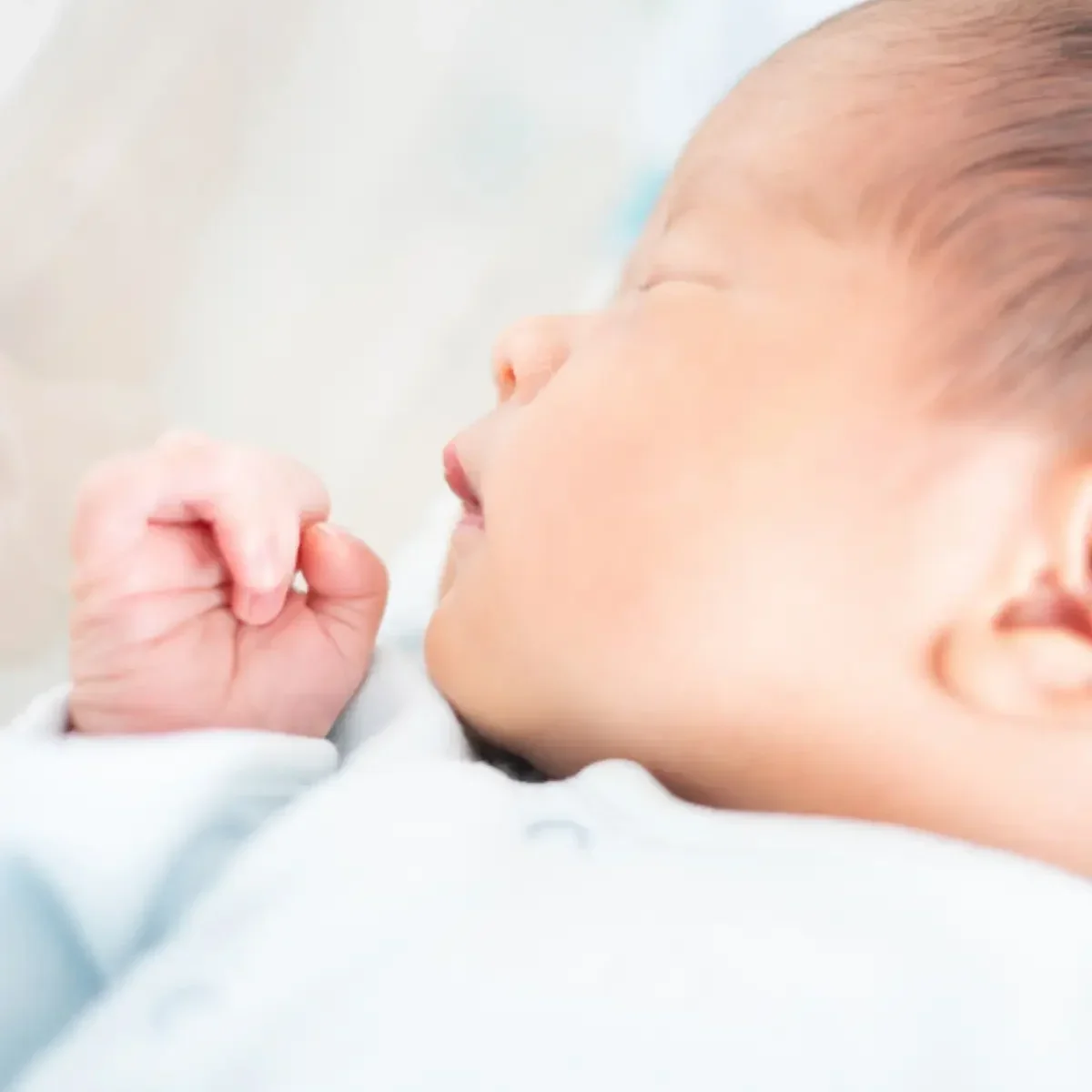 Close-up of sleeping baby with hand near face, wearing white clothing.