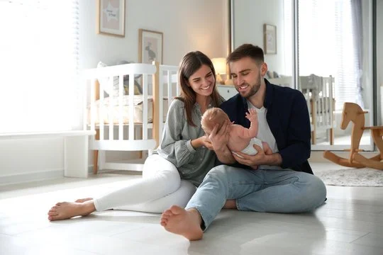 Parents sitting on the floor, holding and smiling at their infant child in a bright nursery room.