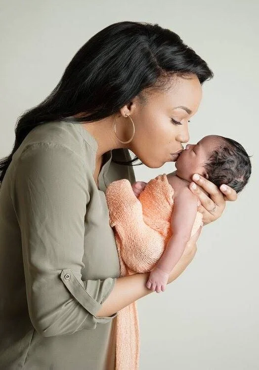 Woman holding and kissing a newborn baby wrapped in a peach blanket.