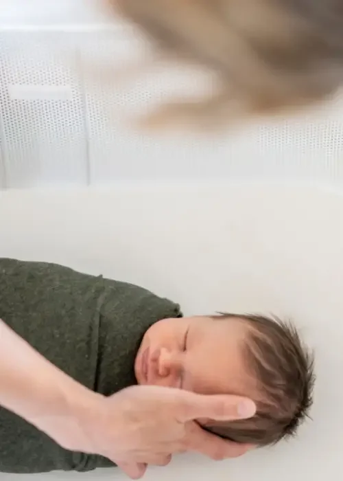 Close-up of a newborn baby sleeping on a soft surface, being gently supported by an adult hand.