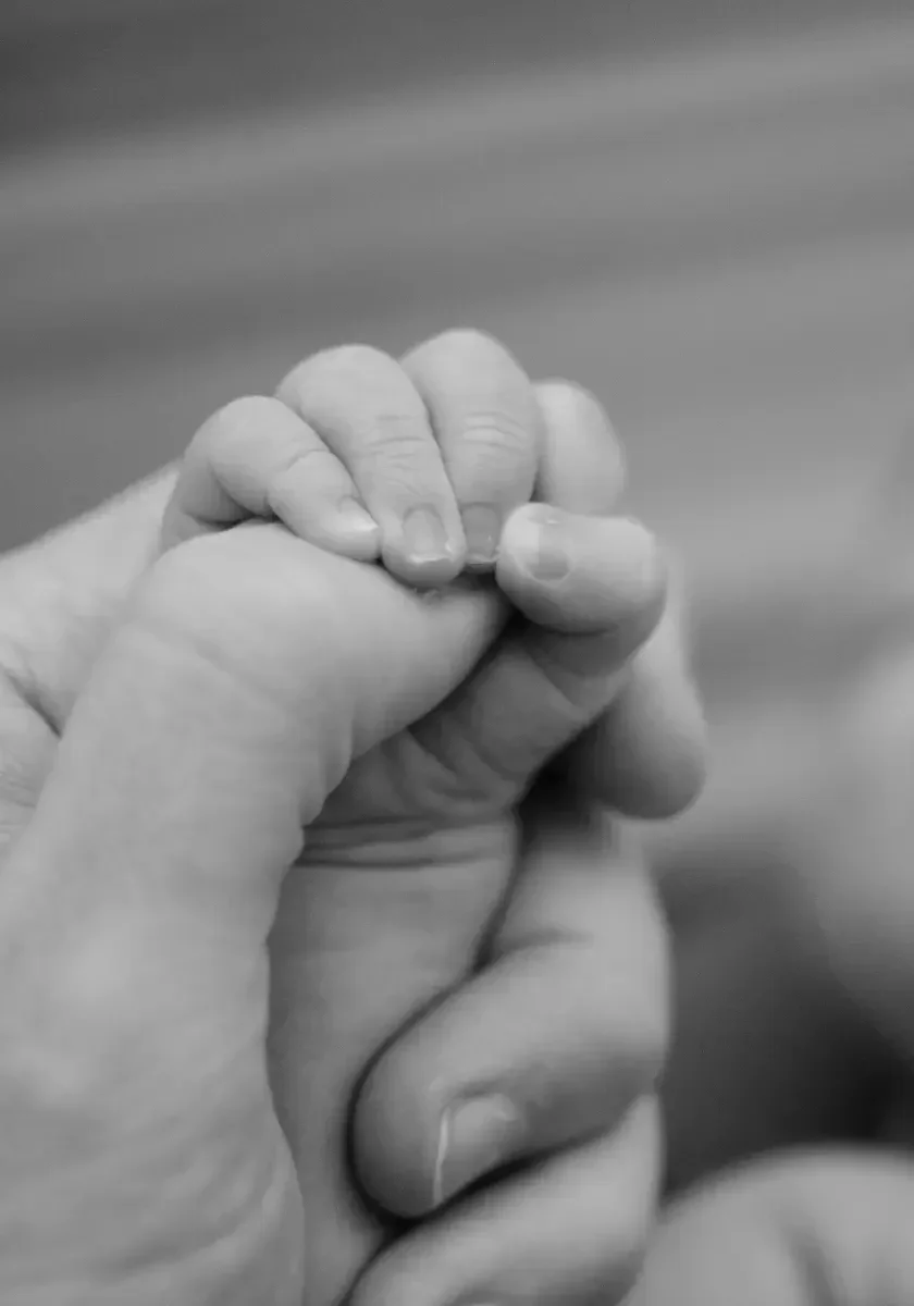 A close-up black and white photograph of an adult hand holding a small child's hand.