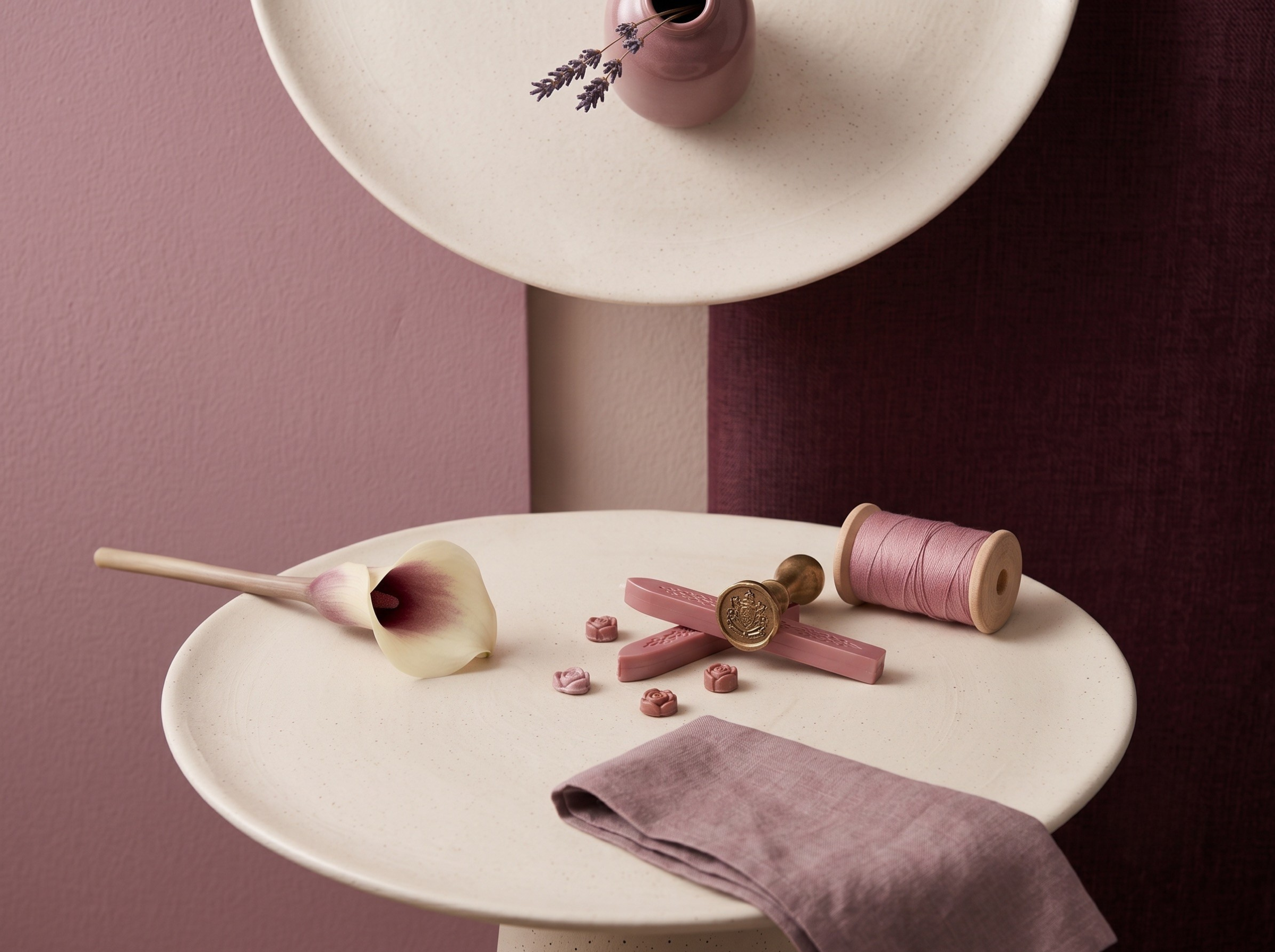 Tablet with pink and gold chocolates, pink spool of thread, pink flower, and purple paper on a white surface against pink and maroon backgrounds.