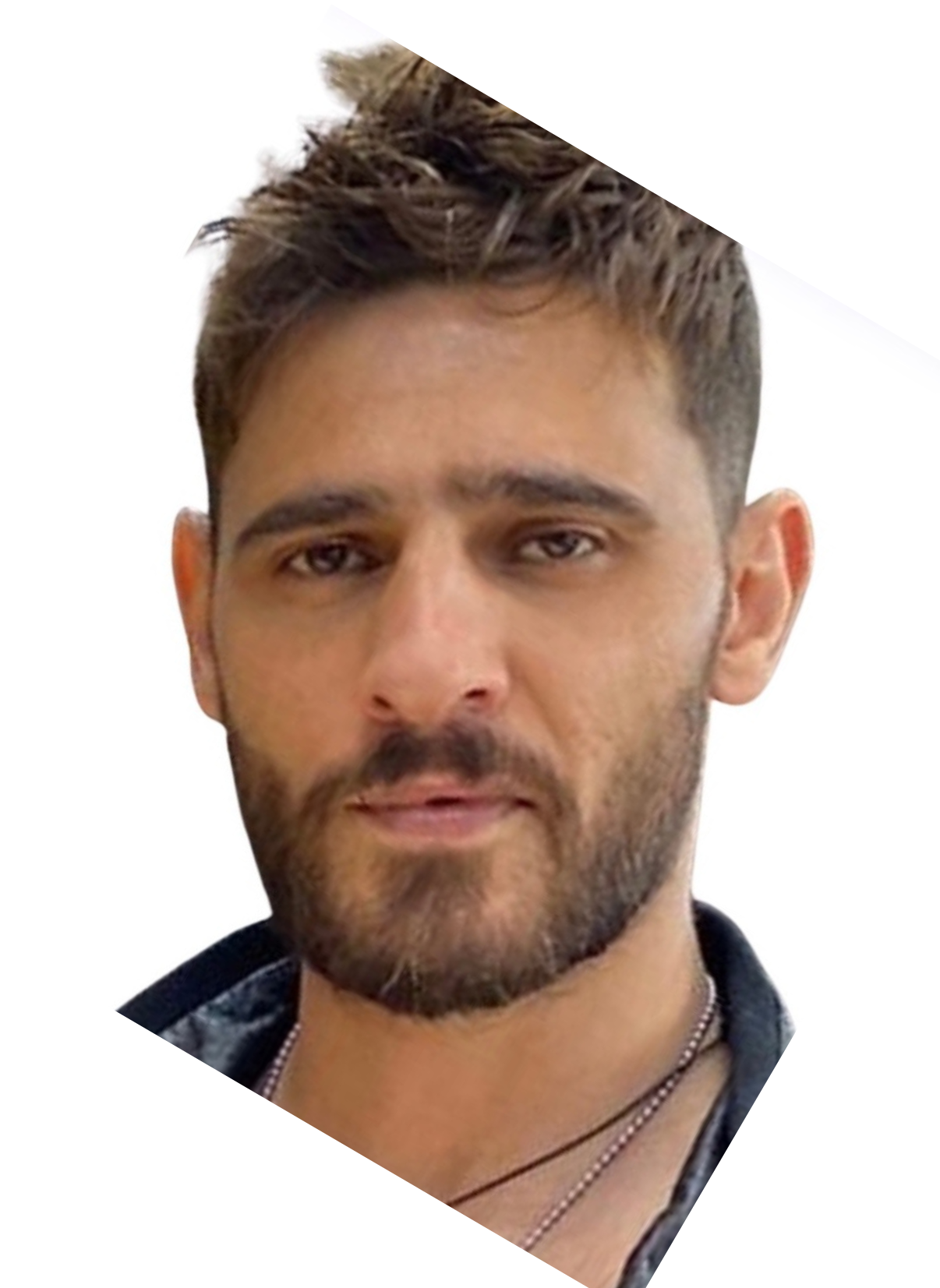 Close-up of a man with short dark brown hair, light brown eyes, and a beard, wearing a necklace and a dark shirt.