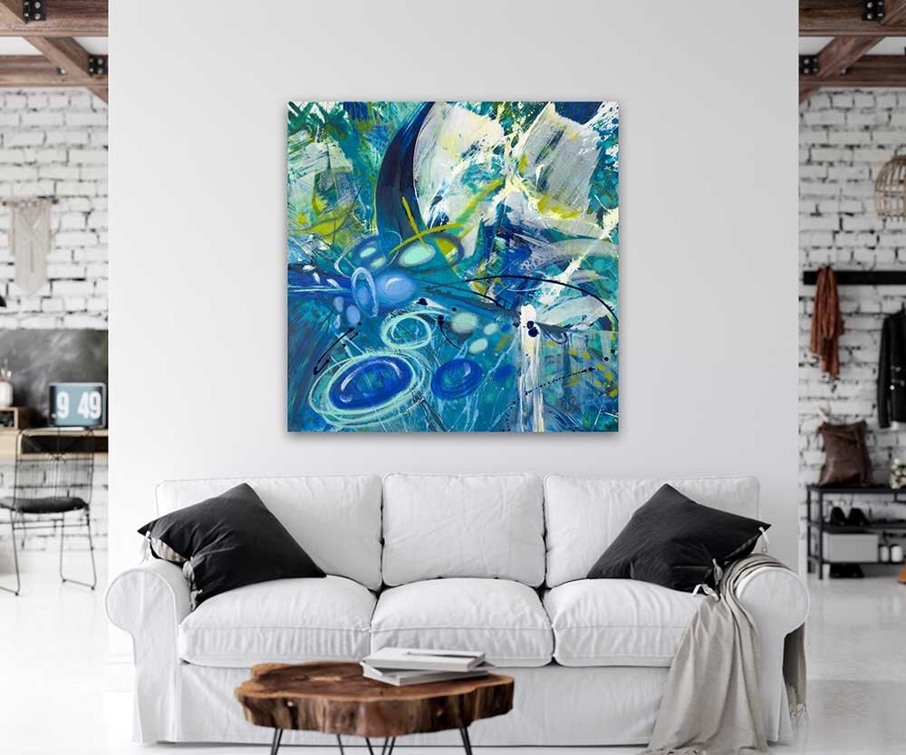 An abstract painting in shades of blue, green, white, and yellow hanging above a white sofa with black pillows in a modern living room.