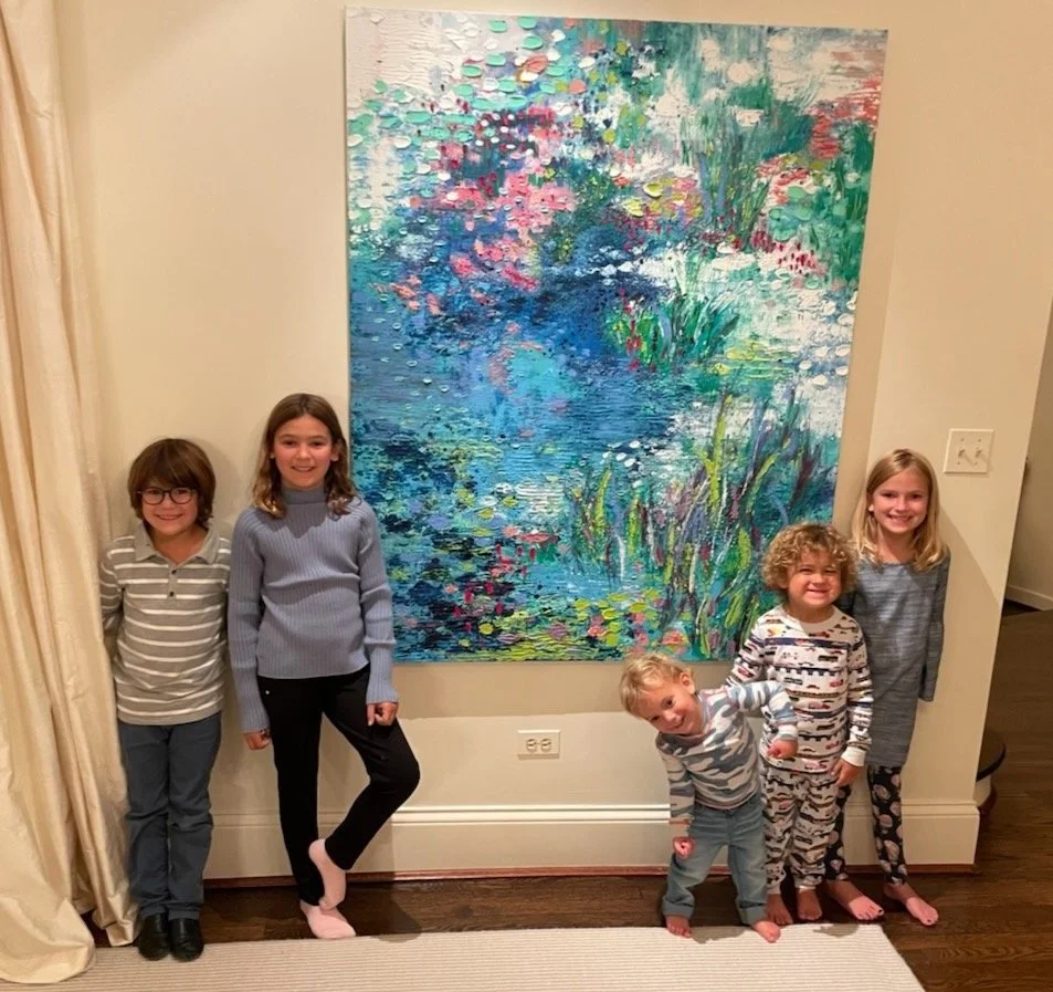 Five children standing in front of a large abstract painting of a pond with water lilies, trees, and colorful reflections, inside a home.