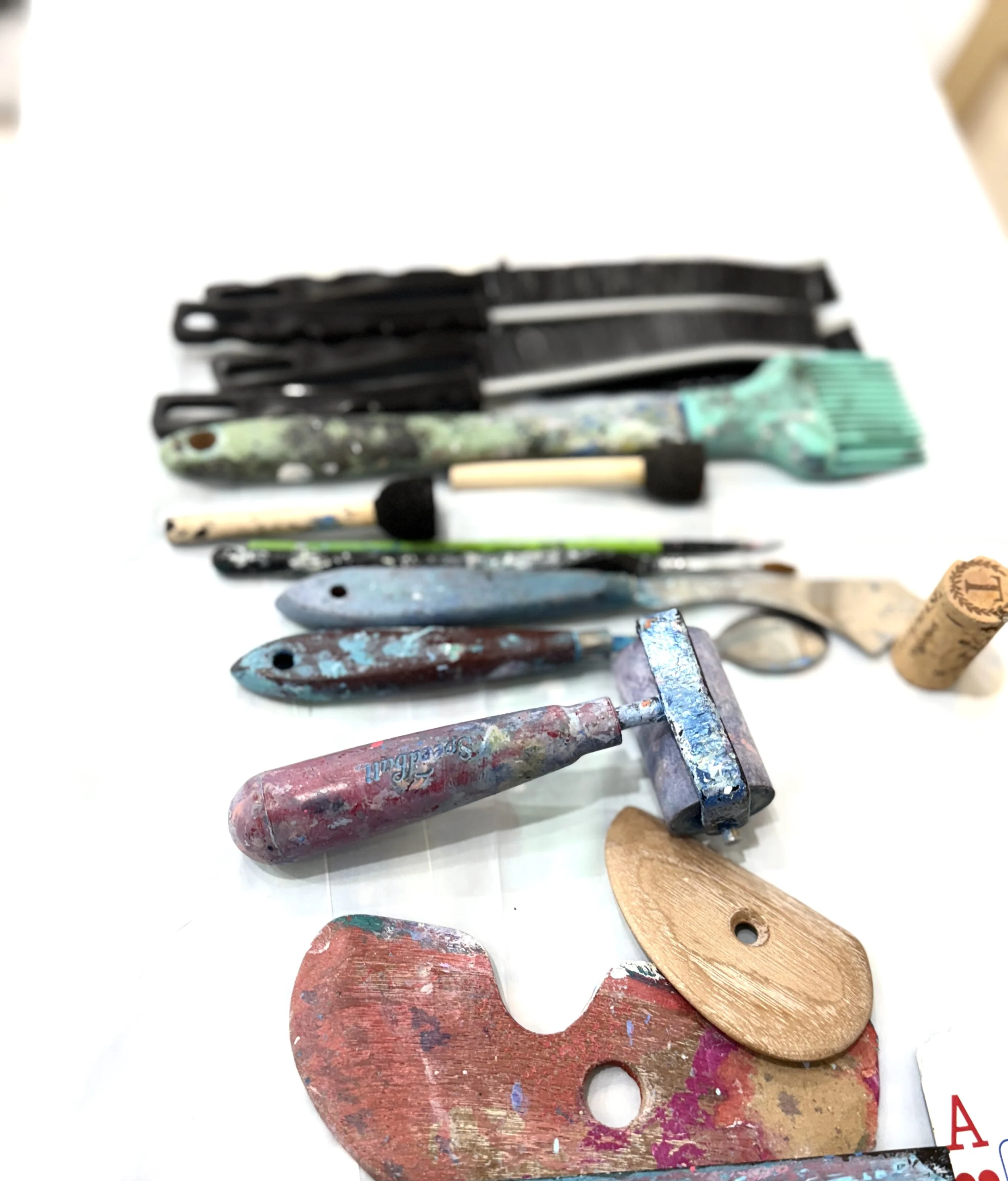 A collection of paint-splattered artist palettes, brushes, and tools on a white surface.