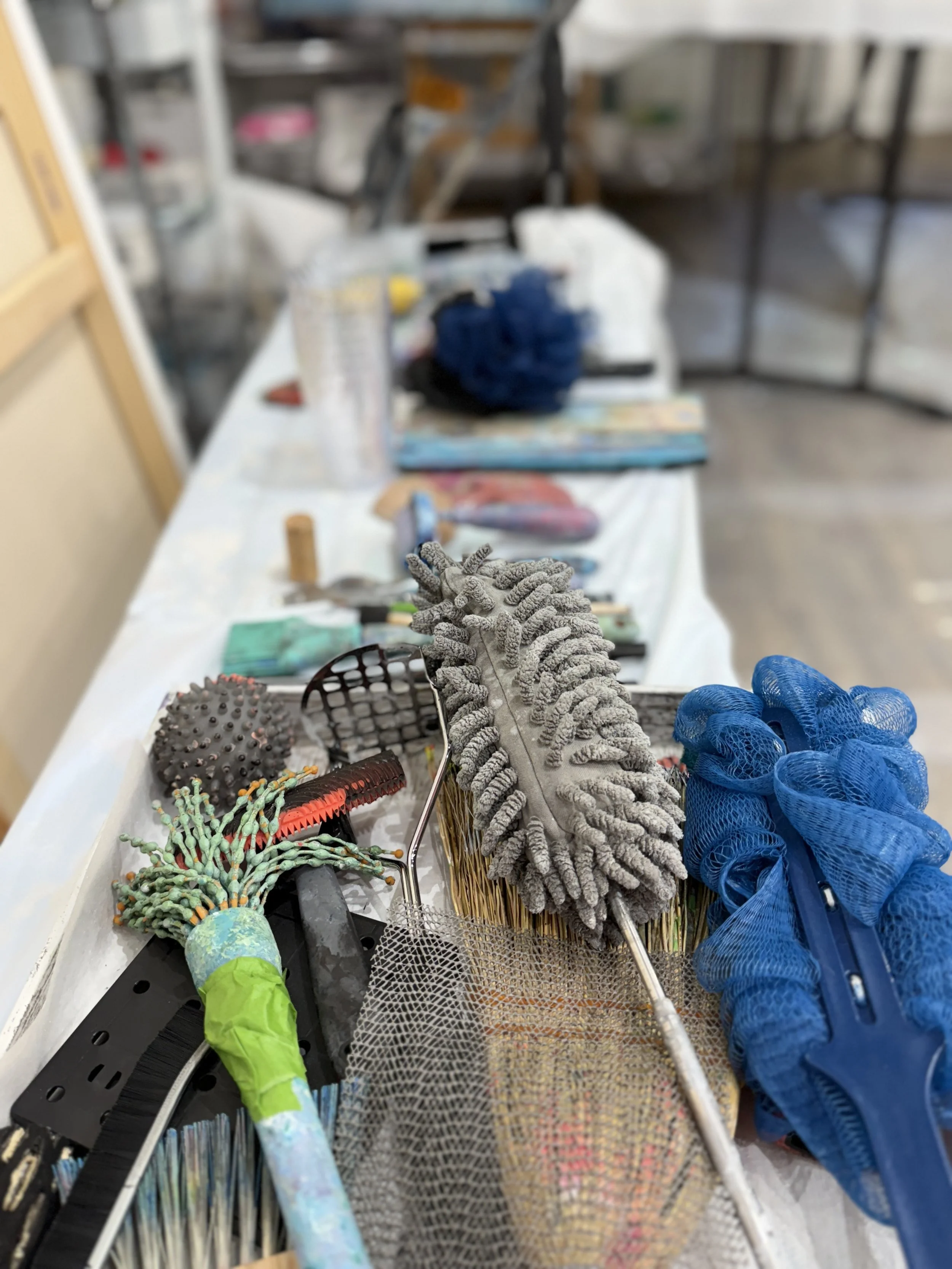 A cluttered lab workspace with various tools and materials, including a mop, gloves, brushes, and containers on a white table.