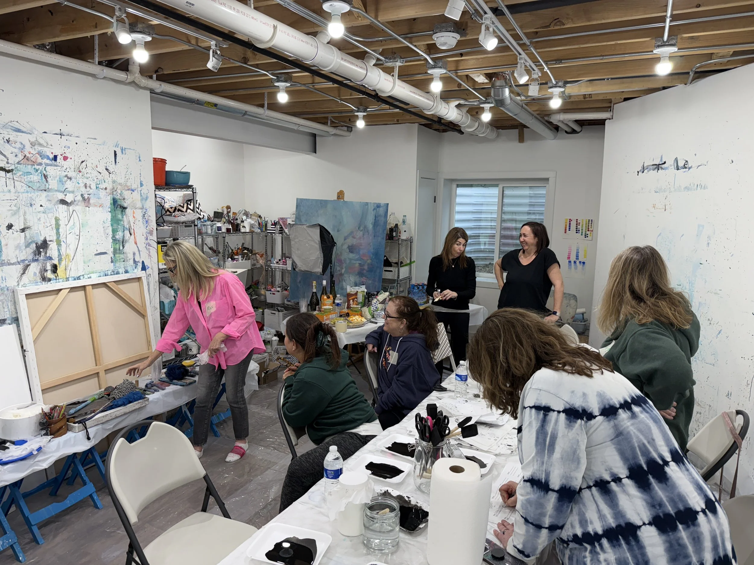 People gathered in an art studio or workshop with paint-splattered walls and tables full of art supplies, participating in an art or craft activity.