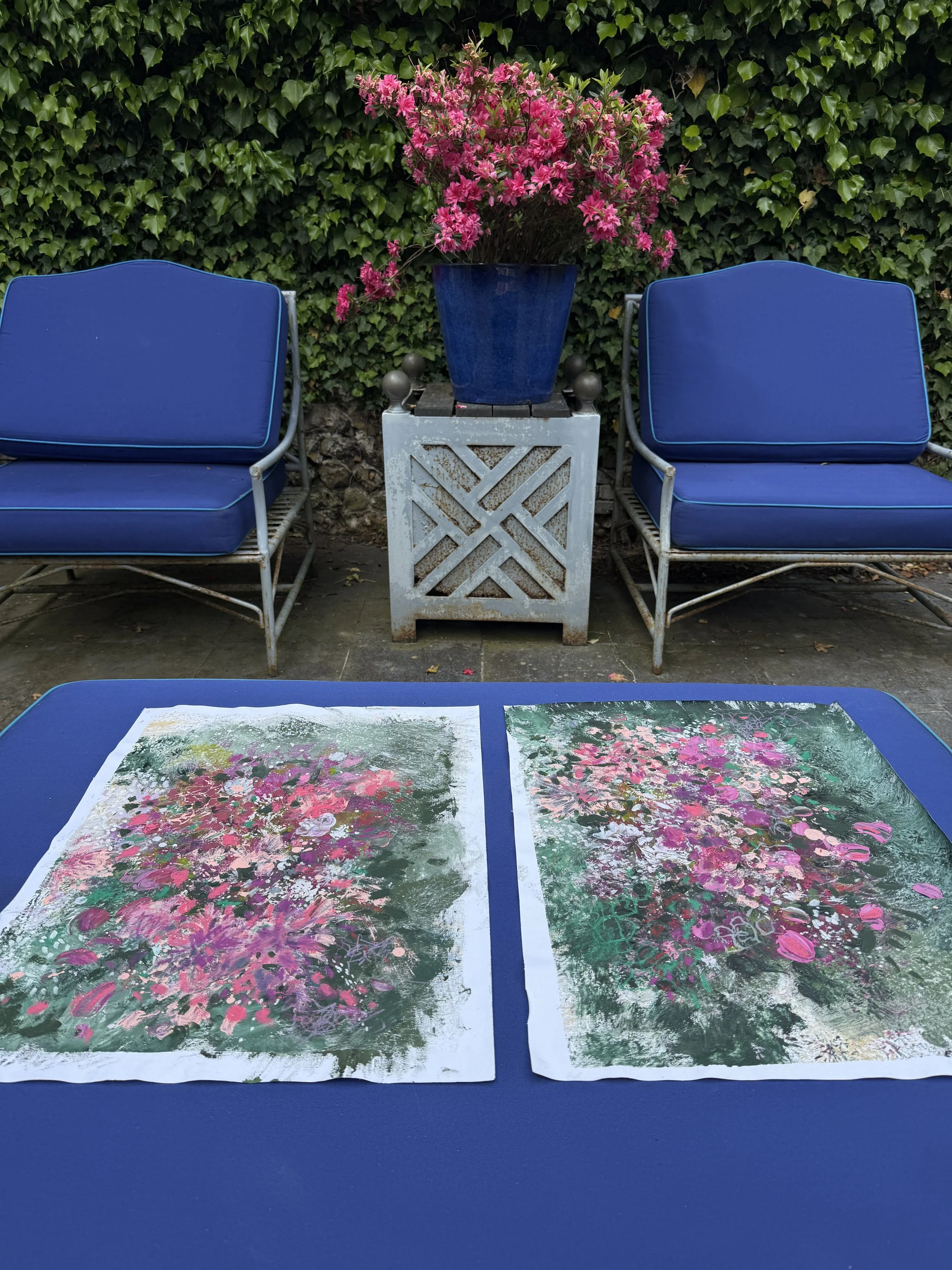 Two abstract paintings with pink and purple flowers on a green background, laid on a blue table.