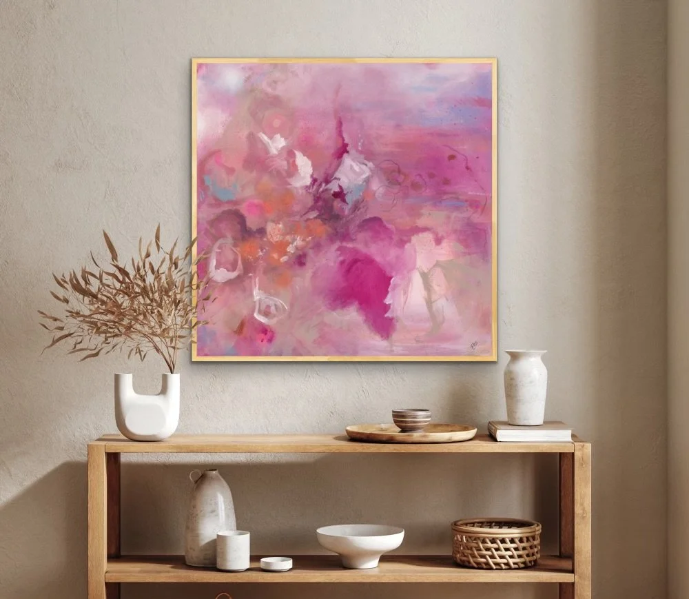 An abstract pink and purple painting hanging above a wooden console table decorated with white and neutral-colored vases and bowls.