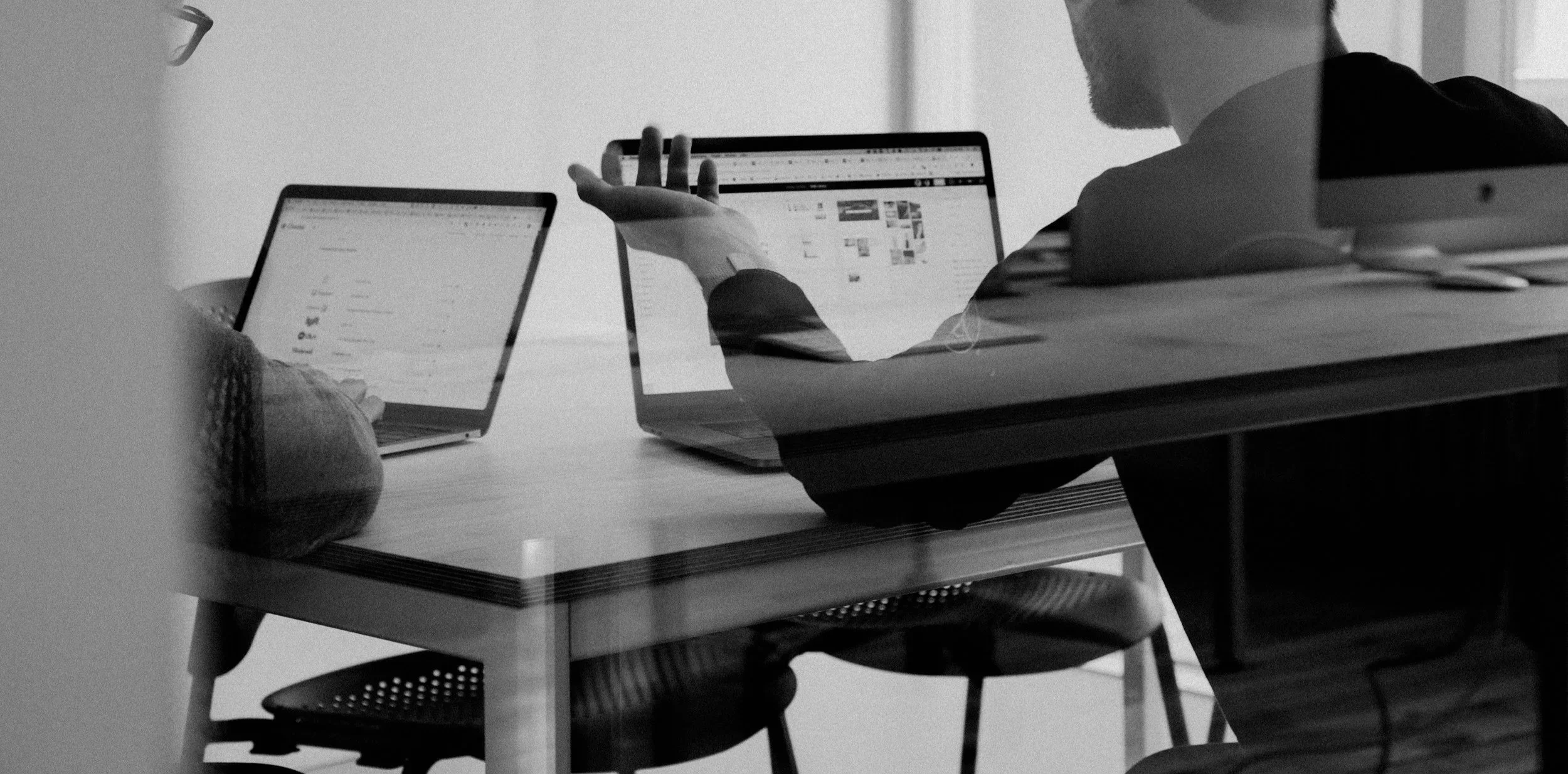 Persona conversando frente a dos computadoras portátiles en un ambiente de oficina.