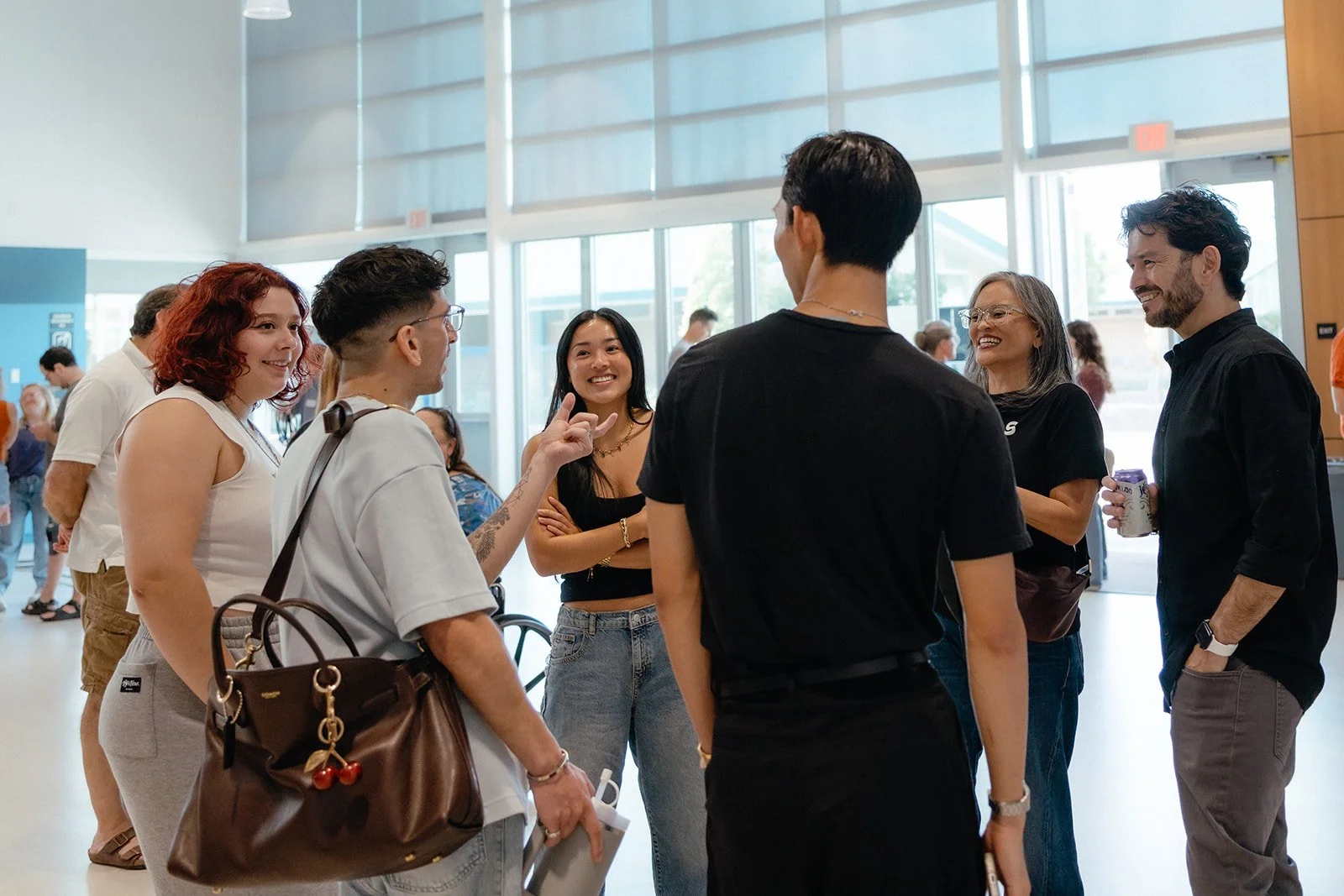 Group of six people gathered and smiling during conversation inside a bright, modern building with large windows.