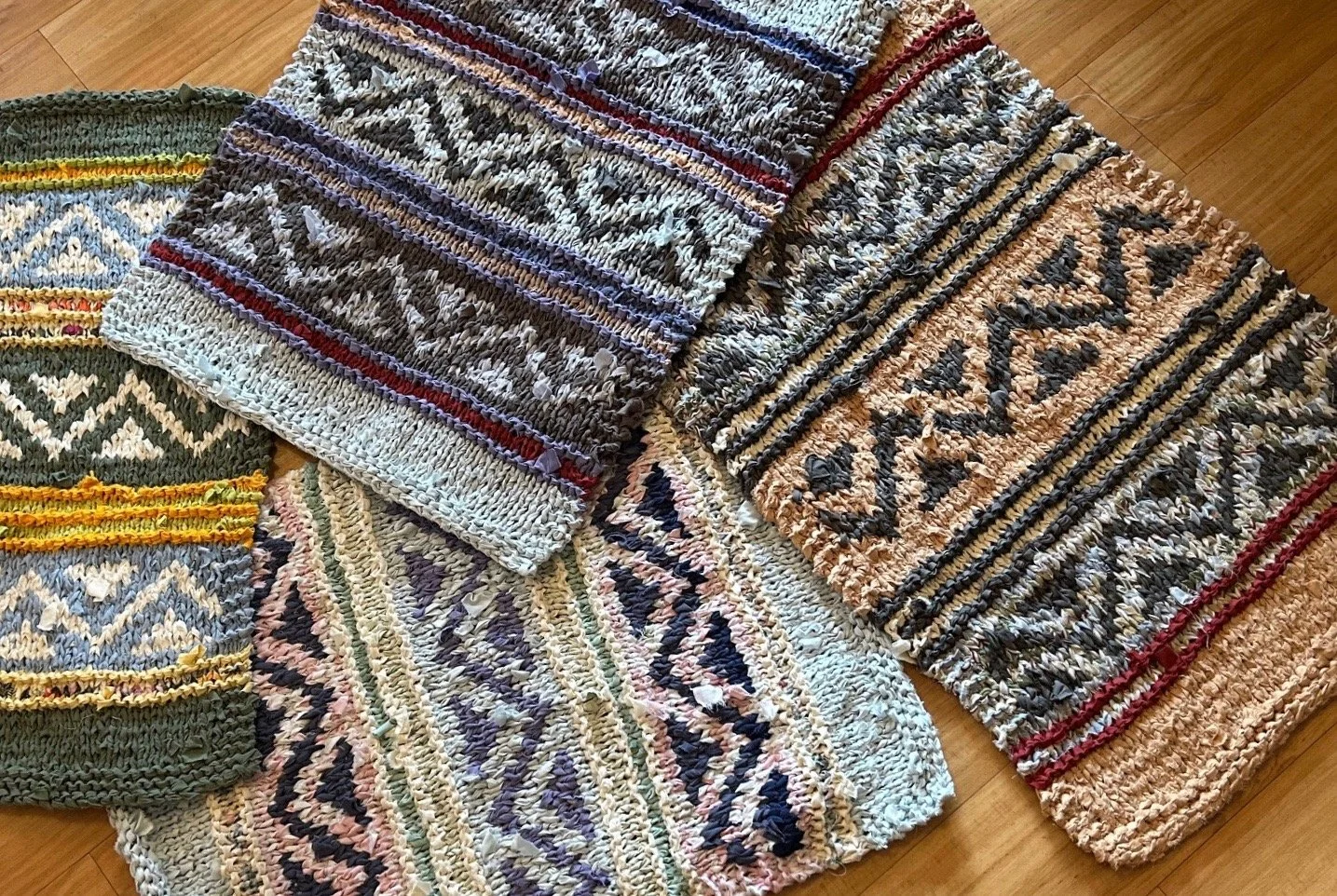 Several handmade woven rugs with colorful geometric patterns are spread out on a wooden floor.