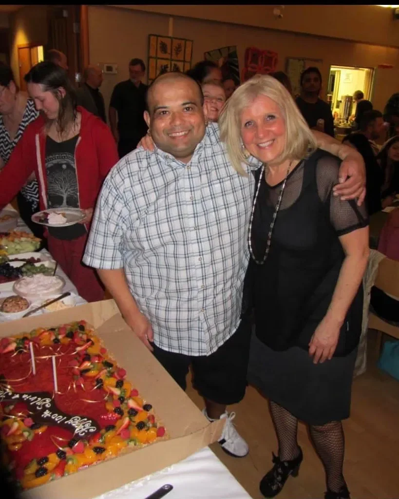 People celebrating around a birthday cake with fruit toppings in a decorated room.