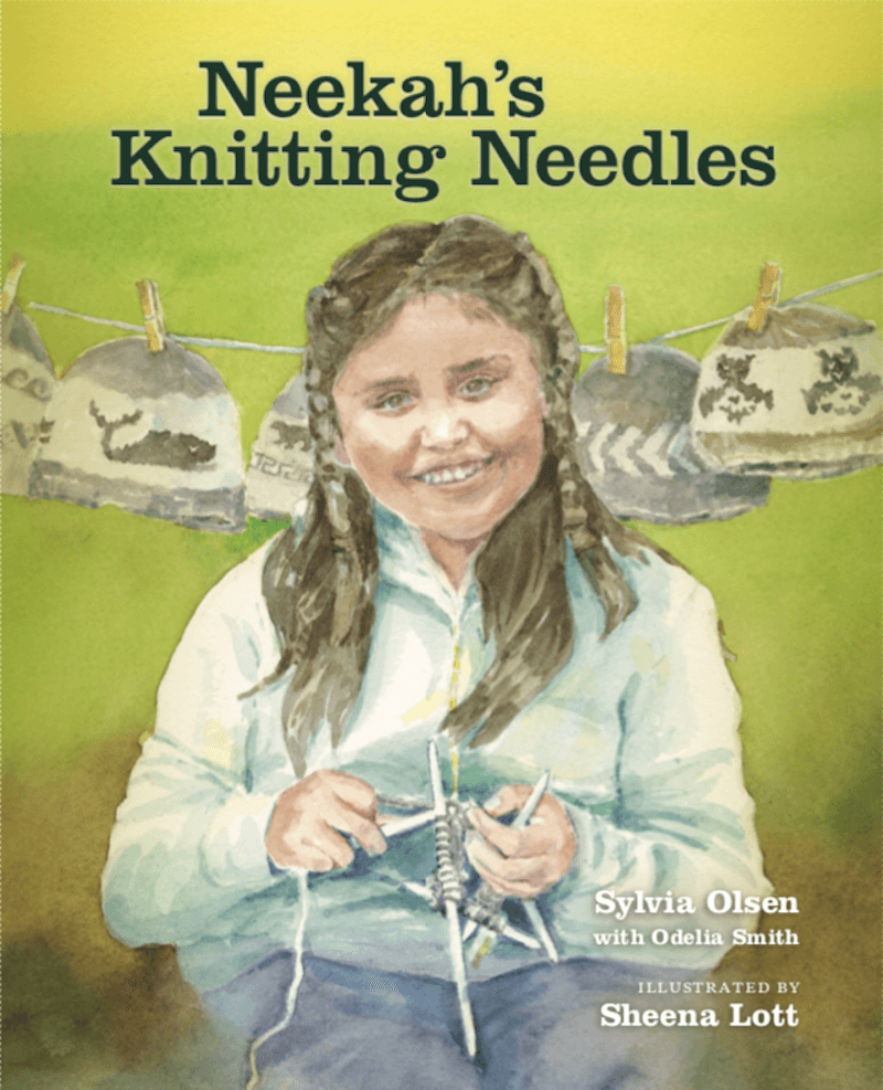 Book cover titled 'Neekah's Knitting Needles.' It features a smiling girl with long brown hair knitting, with a background of a green wall and a clothesline with decorated socks hanging on it. Author Sylvia Olsen with Odelia Smith, illustrated by Sheena Lott.