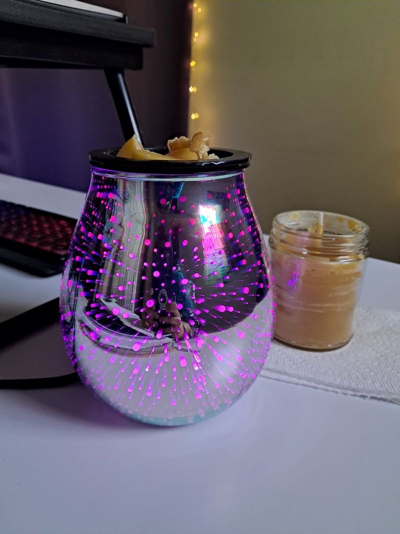 Wax melter with beeswax sits next to a partially filled candle jar