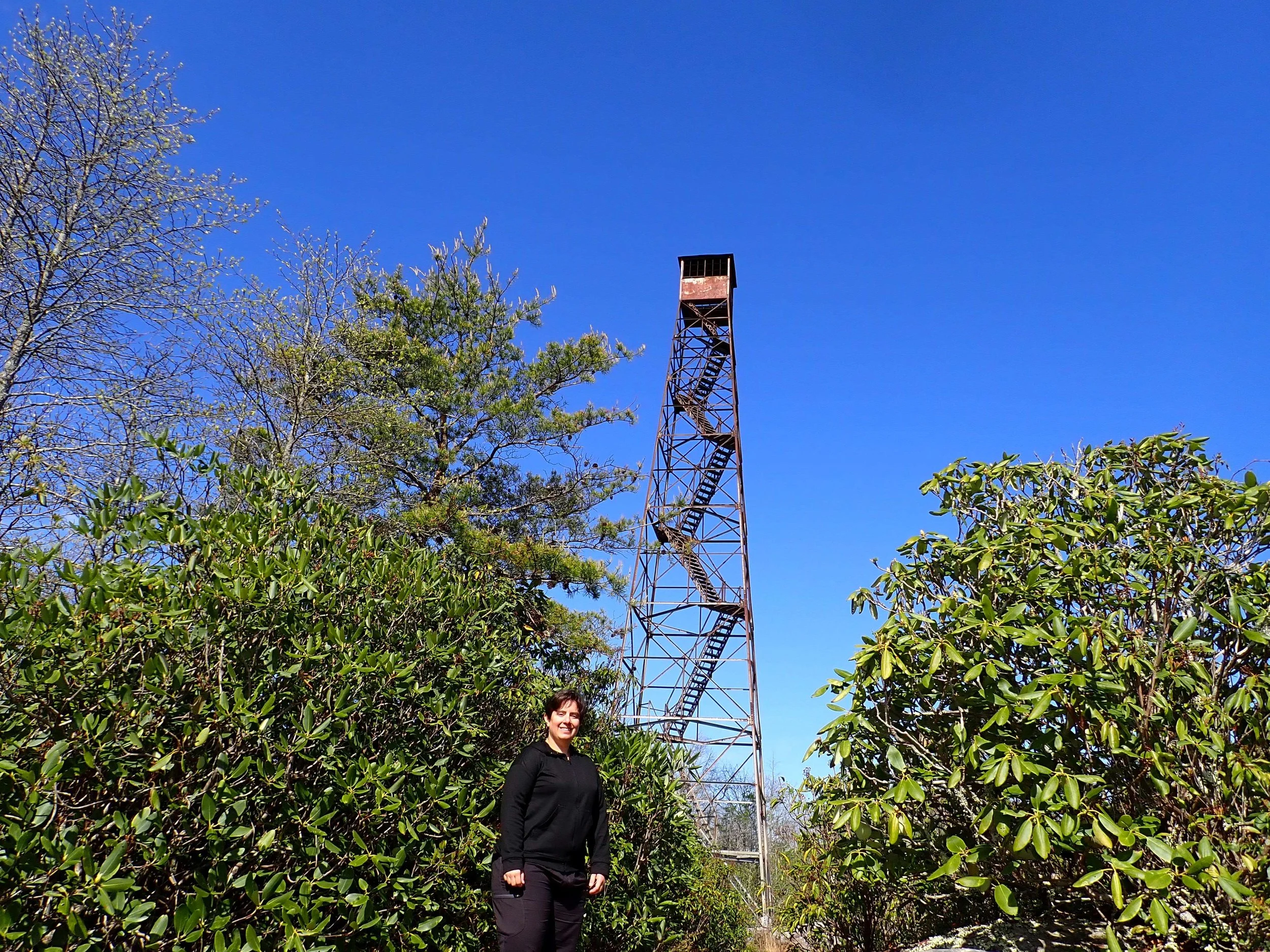 A white woman stands in front of the fire tower at The Channels, VA