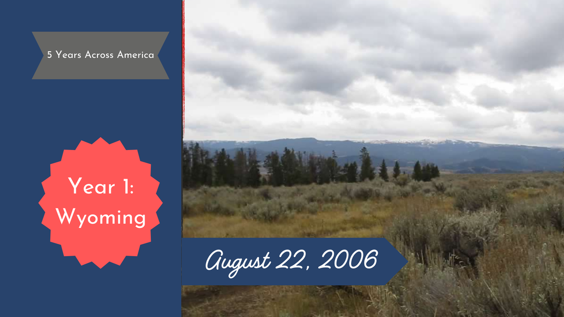 Cloudy skies over a field of sagebrush and evergreen trees with snow-topped mountains in the background