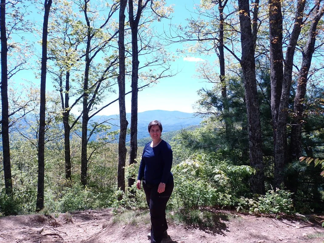 White woman stands on a mountain top in a decidious forest in spring