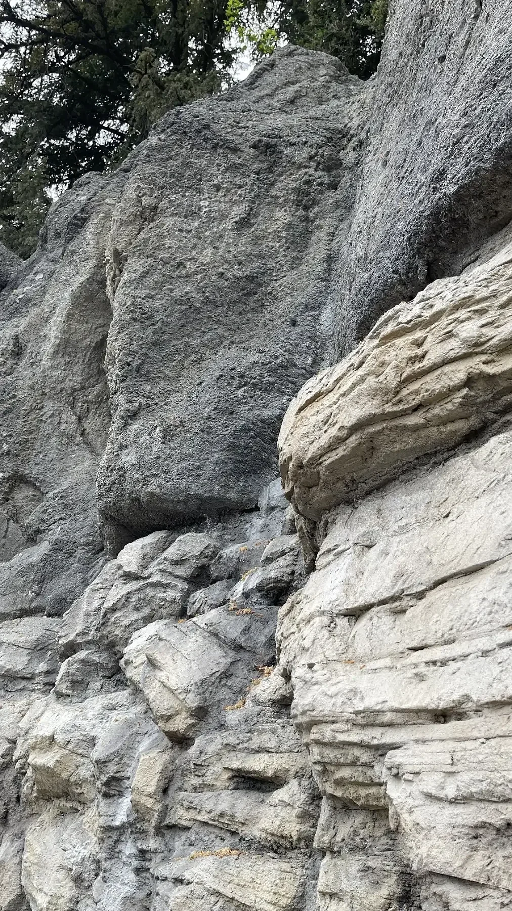 Detail einer künstlich gestalteten Felswand mit unterschiedlichen Gesteinsstrukturen, tiefen Rissen und übereinanderliegenden Felsschichten in Grau- und Beigetönen.