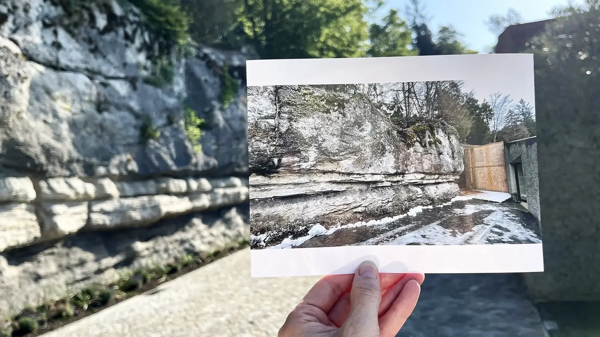 Eine Hand hält ein Foto einer Felswand vor die tatsächliche Felswand. Die Strukturen auf dem Foto stimmen mit dem Hintergrund überein.