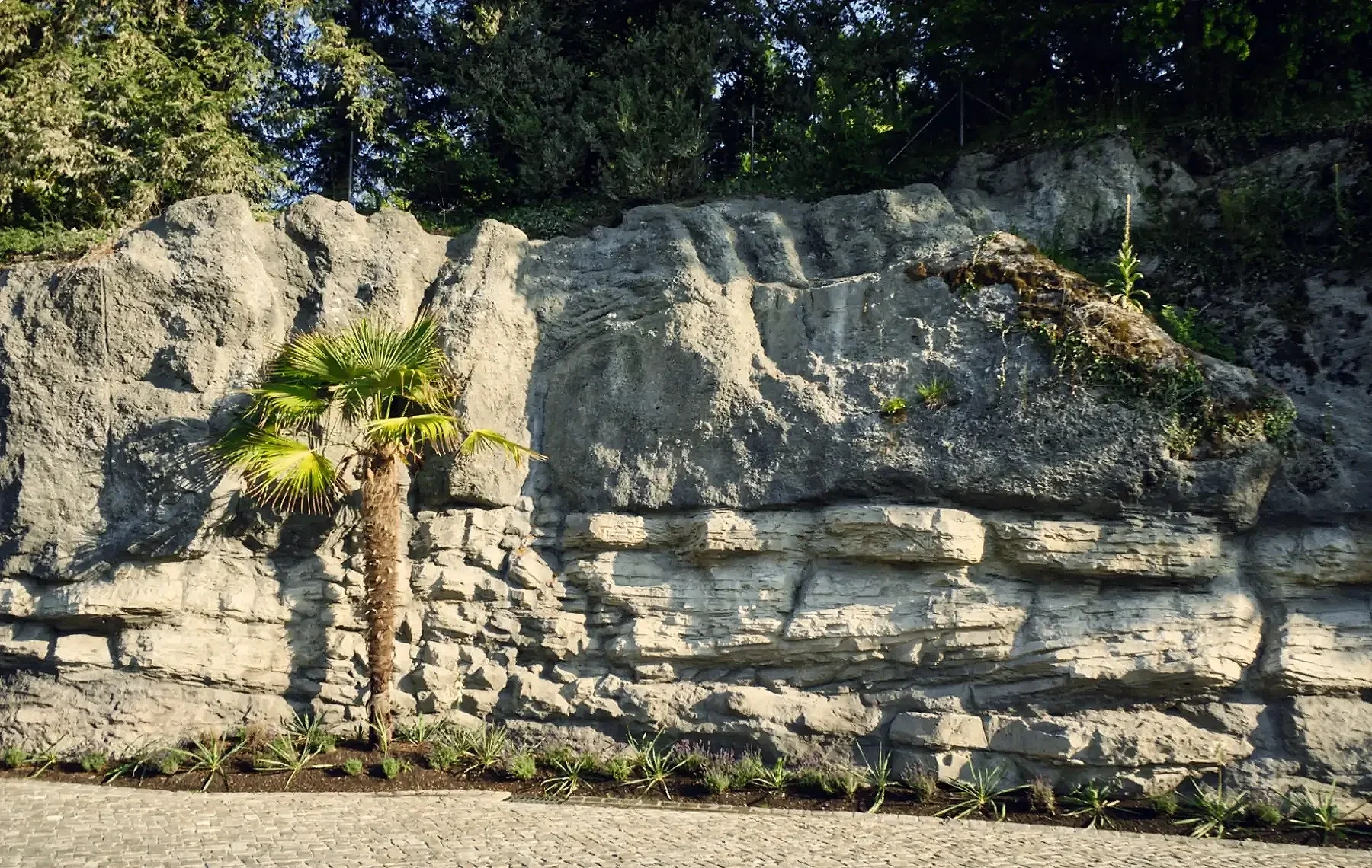 Kunstfelsen mit geschichteter Felsformation, eingebettet in eine gestaltete Gartenlandschaft