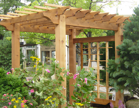 A wooden garden pergola surrounded by colorful flowers and greenery in a yard.