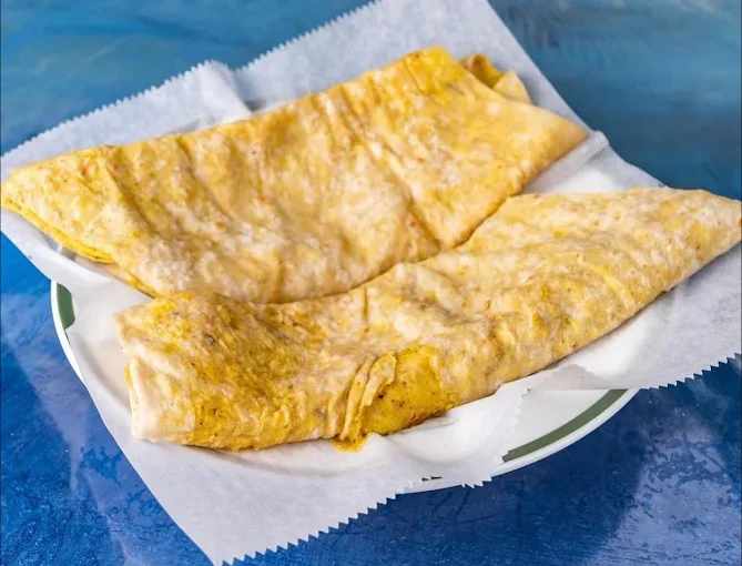 Two folded breakfast burritos on a plate lined with paper, placed on a blue surface.