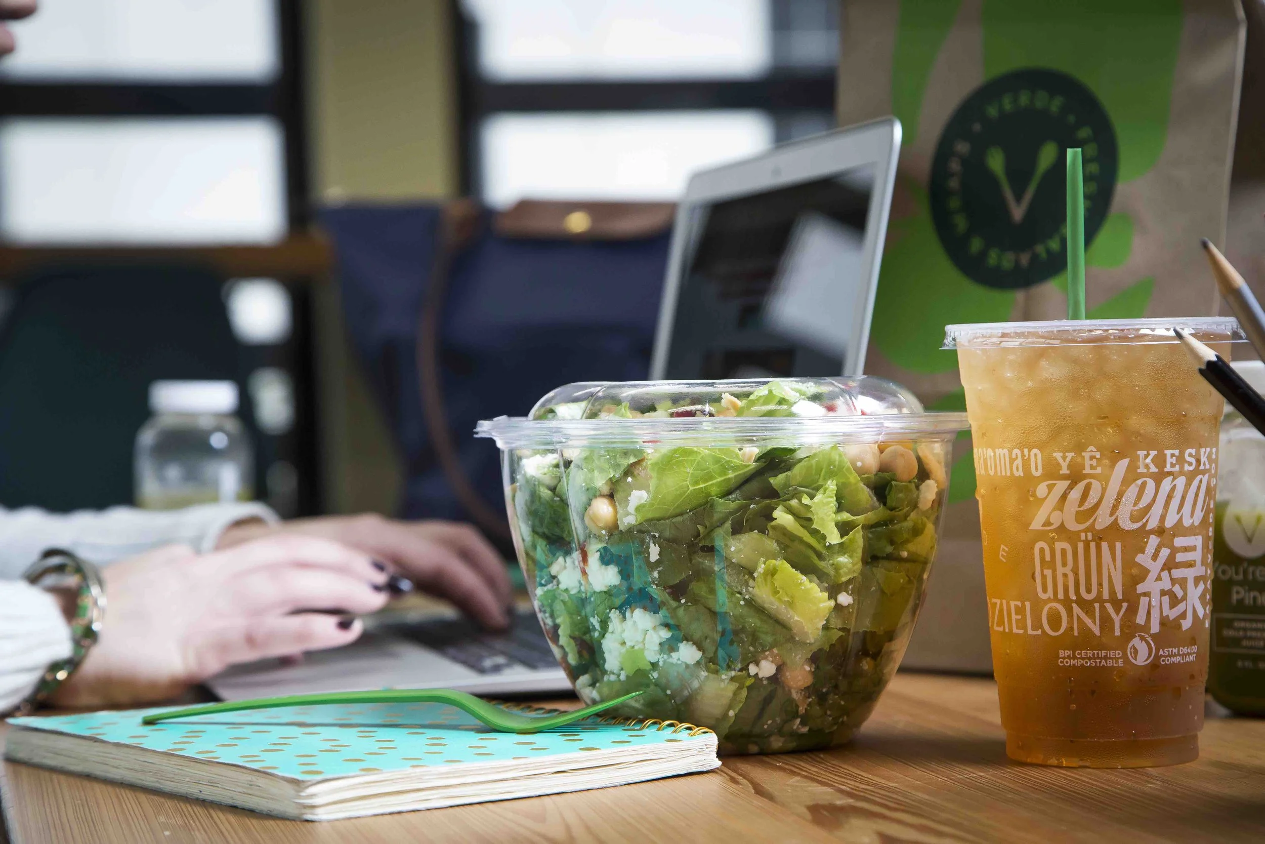 A woman seated at a desk with a laptop and a salad, showcasing Verde's commitment to fresh greens in Charleston, SC.