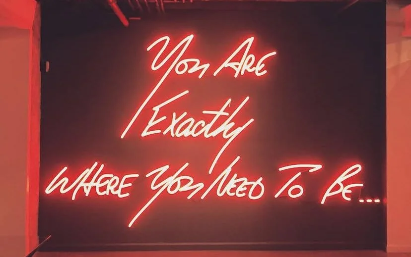 Neon sign with the quote 'You Are Exactly Where You Need To Be' in red cursive letters.