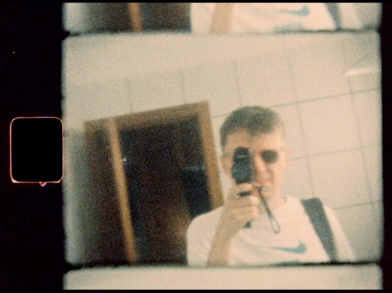 A young man with sunglasses taking a selfie with his super 8 film camera.