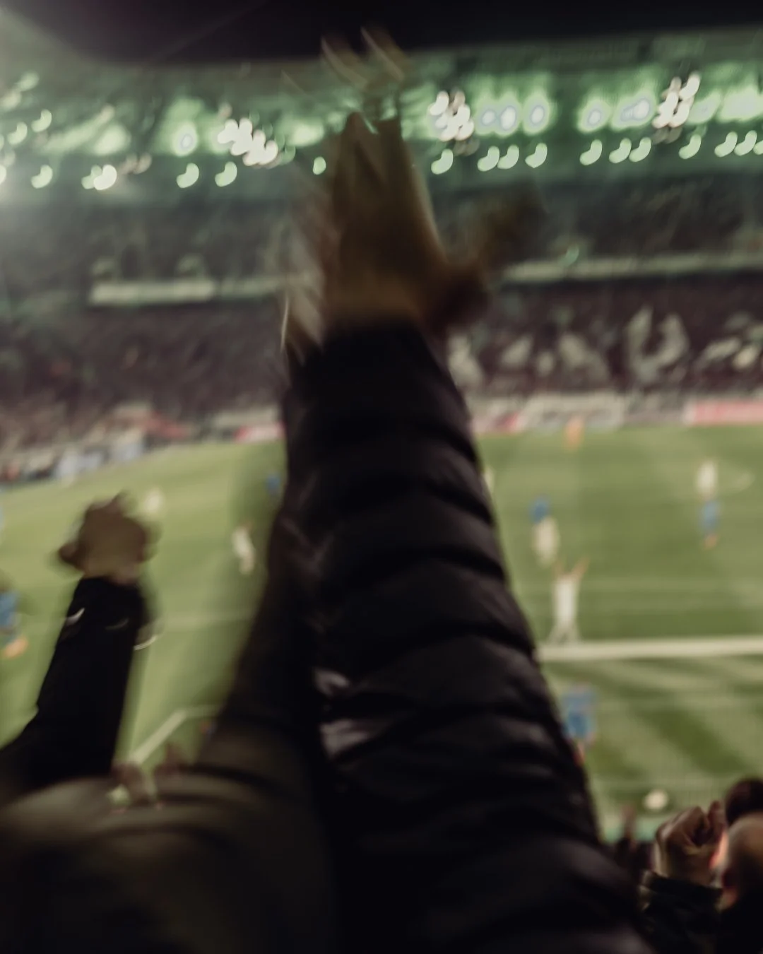 Person's arm and hand pointing towards football players on a field at a stadium during a game.