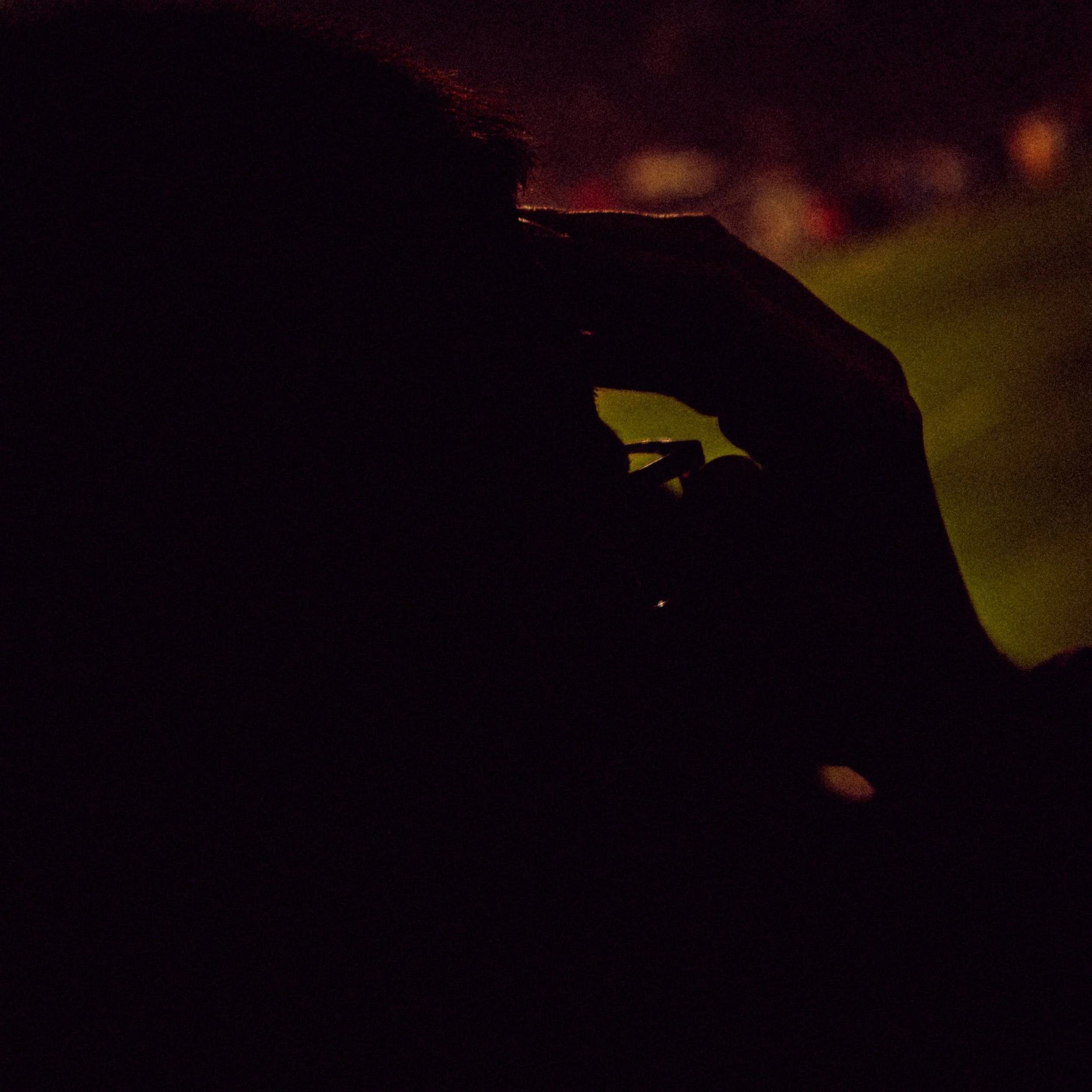 A dark nighttime scene with faint, colorful lights in the distance, partially obscured by darkness and rain droplets on the camera lens.