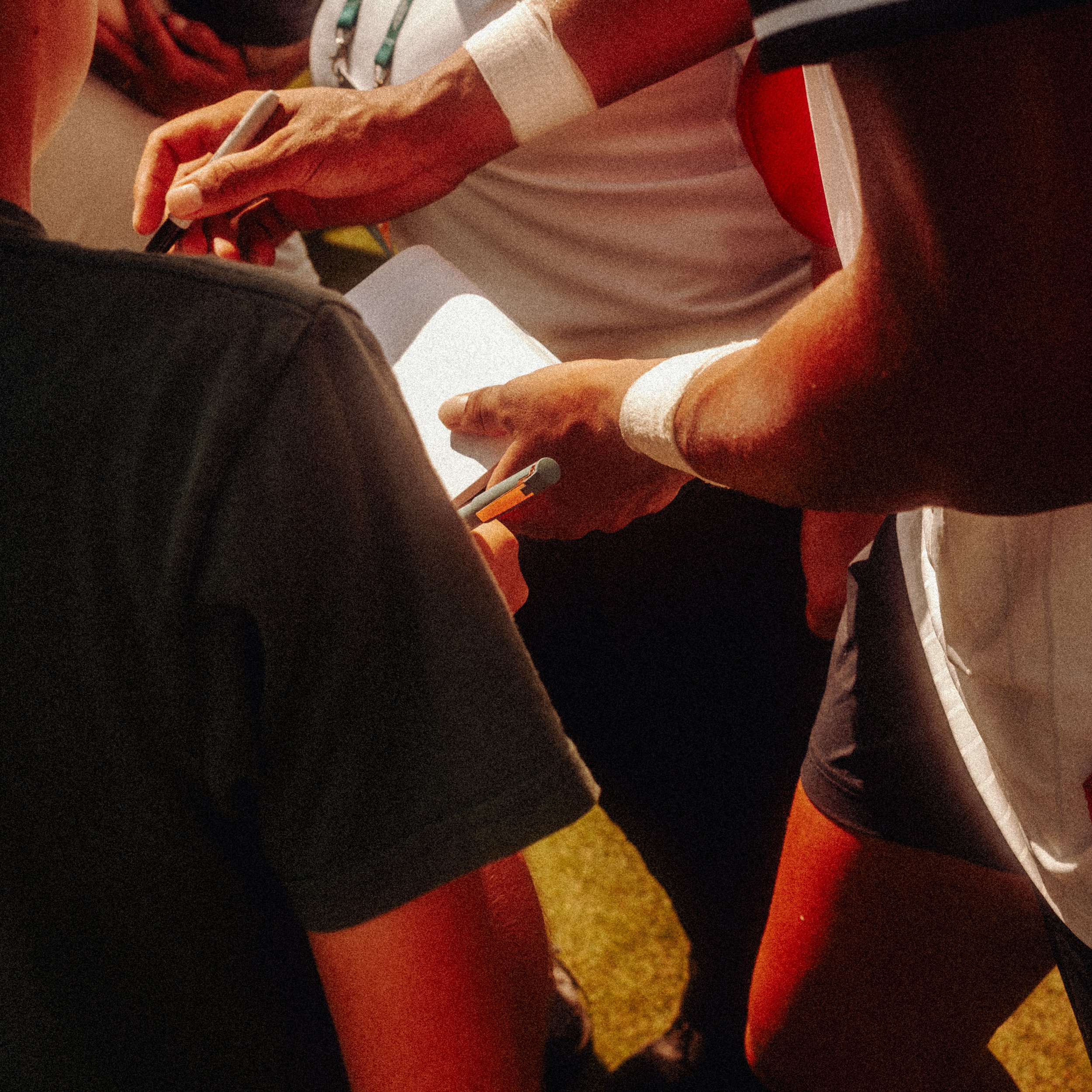 Close-up of a person writing on a notepad at a table, with another hand holding a pen nearby, in a setting with athletic and vibrant table markings.