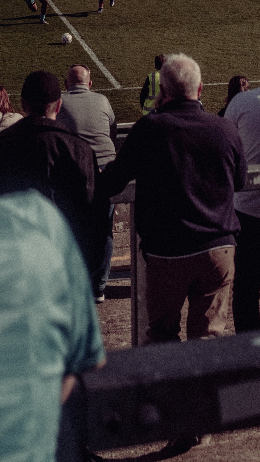 Spectators watching a soccer match on a field at night, with a soccer ball and players visible in the background.